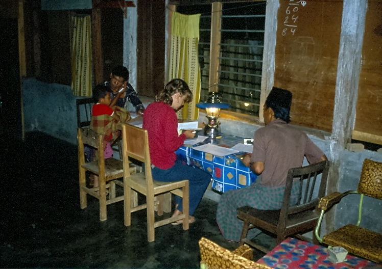 B. Röttger-Rössler beim abendlichen Protokollschreiben im Feld bei Petromax Lampe und mit Forschungsteilnehmenden an der Seite, die alles kommentierten, was geschrieben wurde, 1984, Martin Rössler, All rights reserved